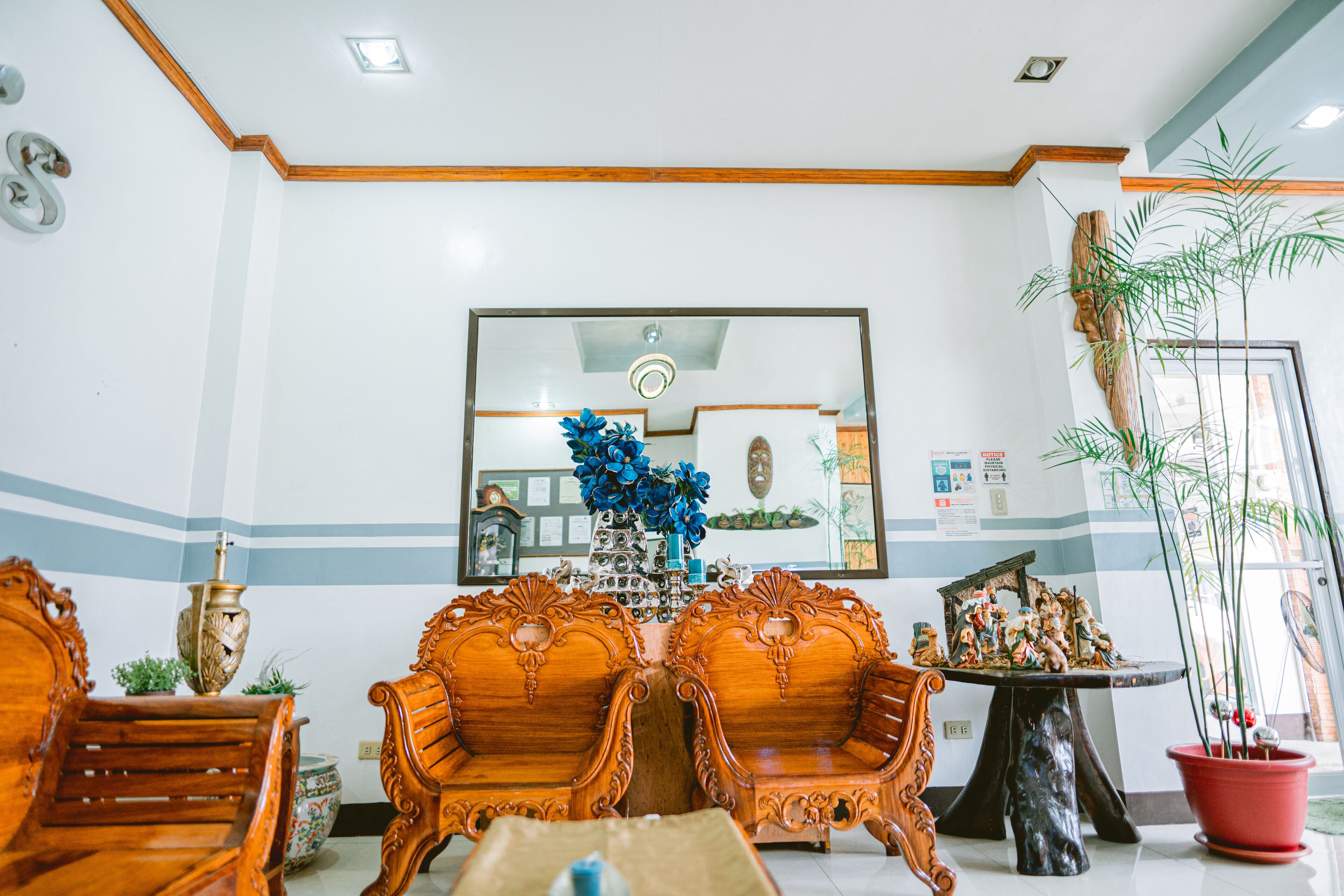 A lobby with wooden chairs, a table with a vase of flowers, and a large mirror on the wall.