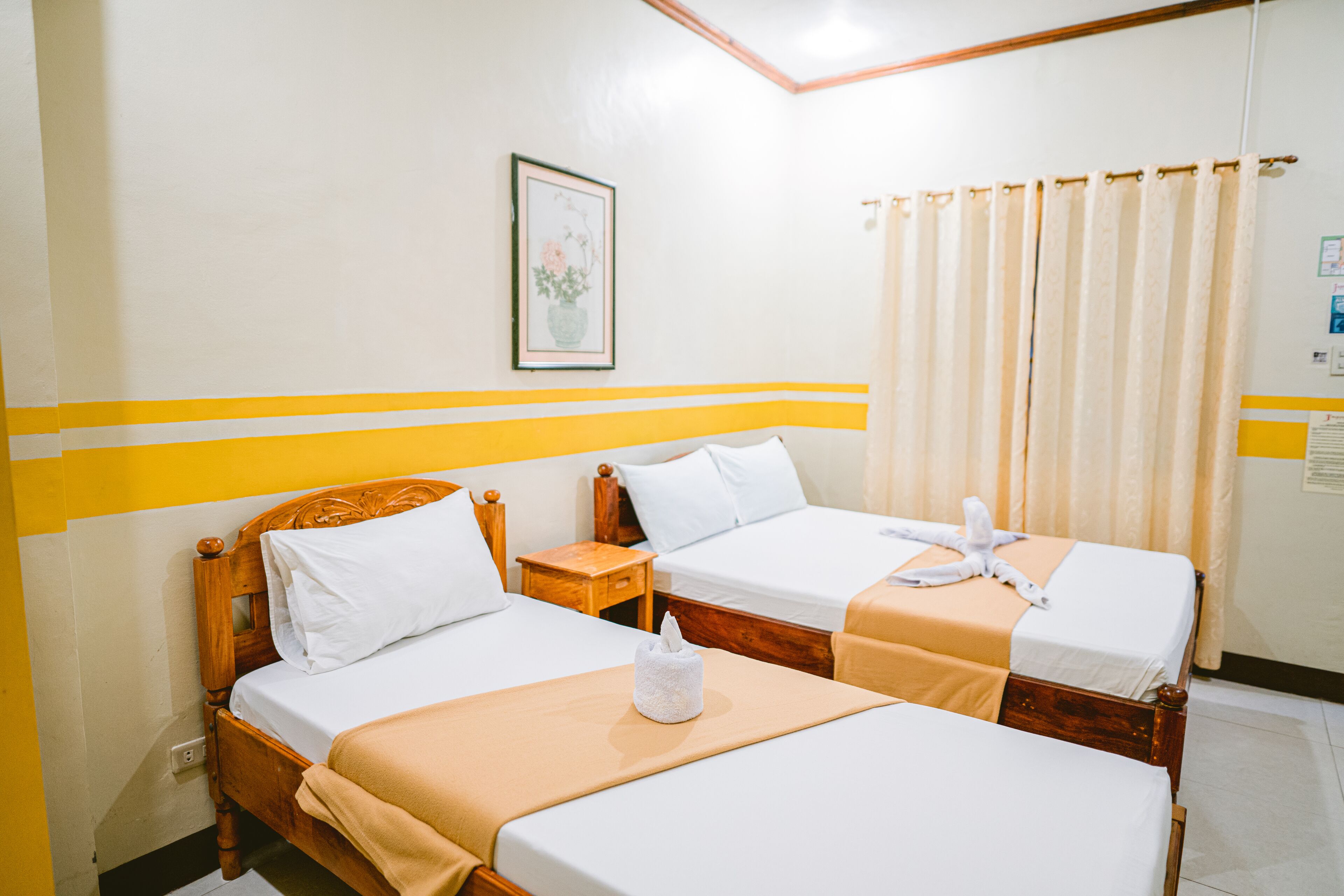 A hotel room with two single beds, wooden headboards, white linens, and a yellow-striped wall design.