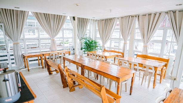 A spacious dining area with wooden tables and chairs, large windows with curtains, and a potted plant. - Jazmine's Place (Coron)