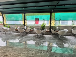 Un área de estar interior moderna con suelo de vidrio, sillas blancas y plantas en macetas.