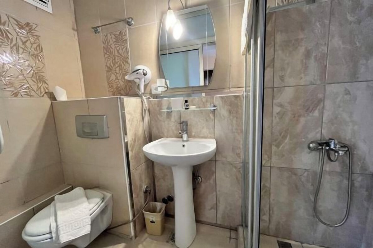 A bathroom with a pedestal sink, a handheld showerhead, a towel rack, and a mirror.