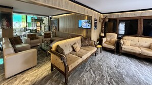 Un salón amplio con un sofá grande, sillones y una mesa de centro. Hay un televisor montado en la pared y un jarrón decorativo sobre una mesita.