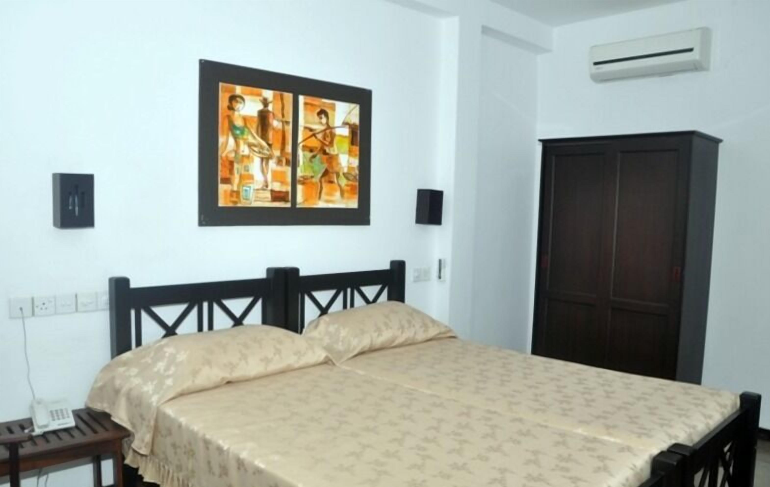 A bedroom with a bed, a wardrobe, a painting on the wall, and an air conditioning unit.