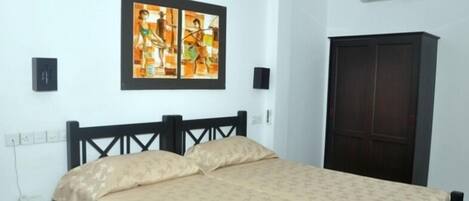 A bedroom with a bed, a wardrobe, a painting on the wall, and an air conditioning unit.