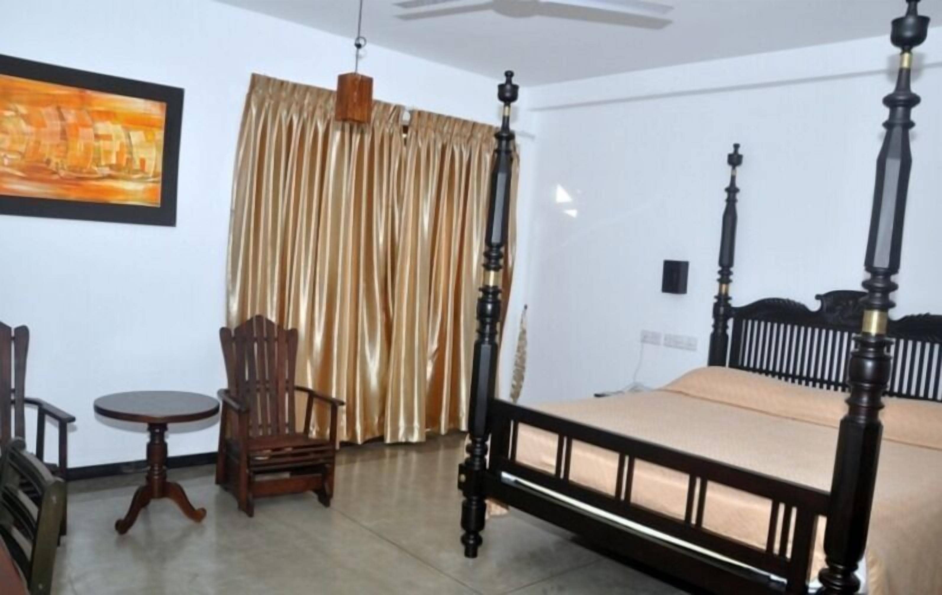 A room with a four-poster bed, a wooden chair, a small round table, and a painting on the wall.