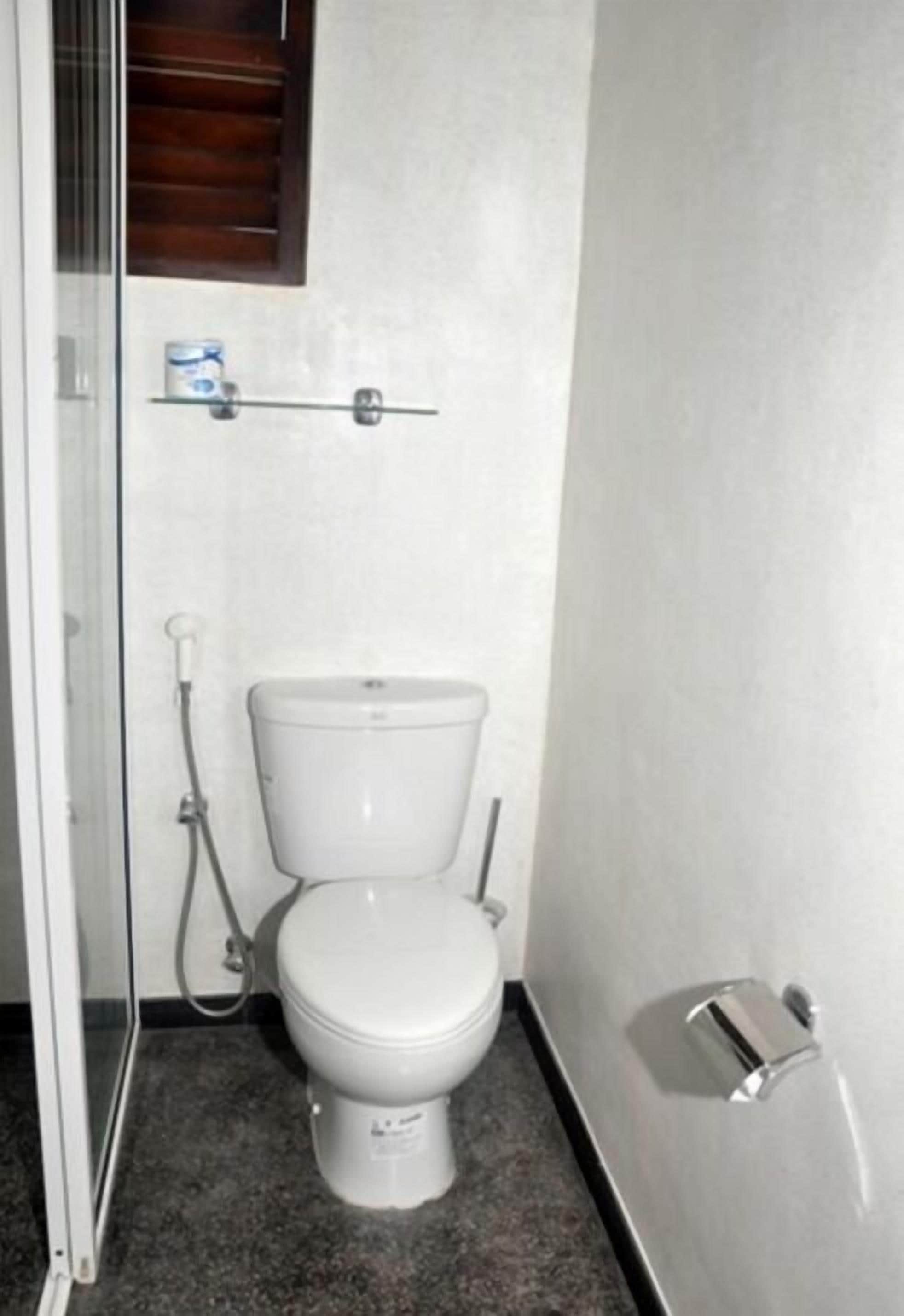 A small, compact bathroom with a white toilet, a shower area, and a small shelf above the toilet.