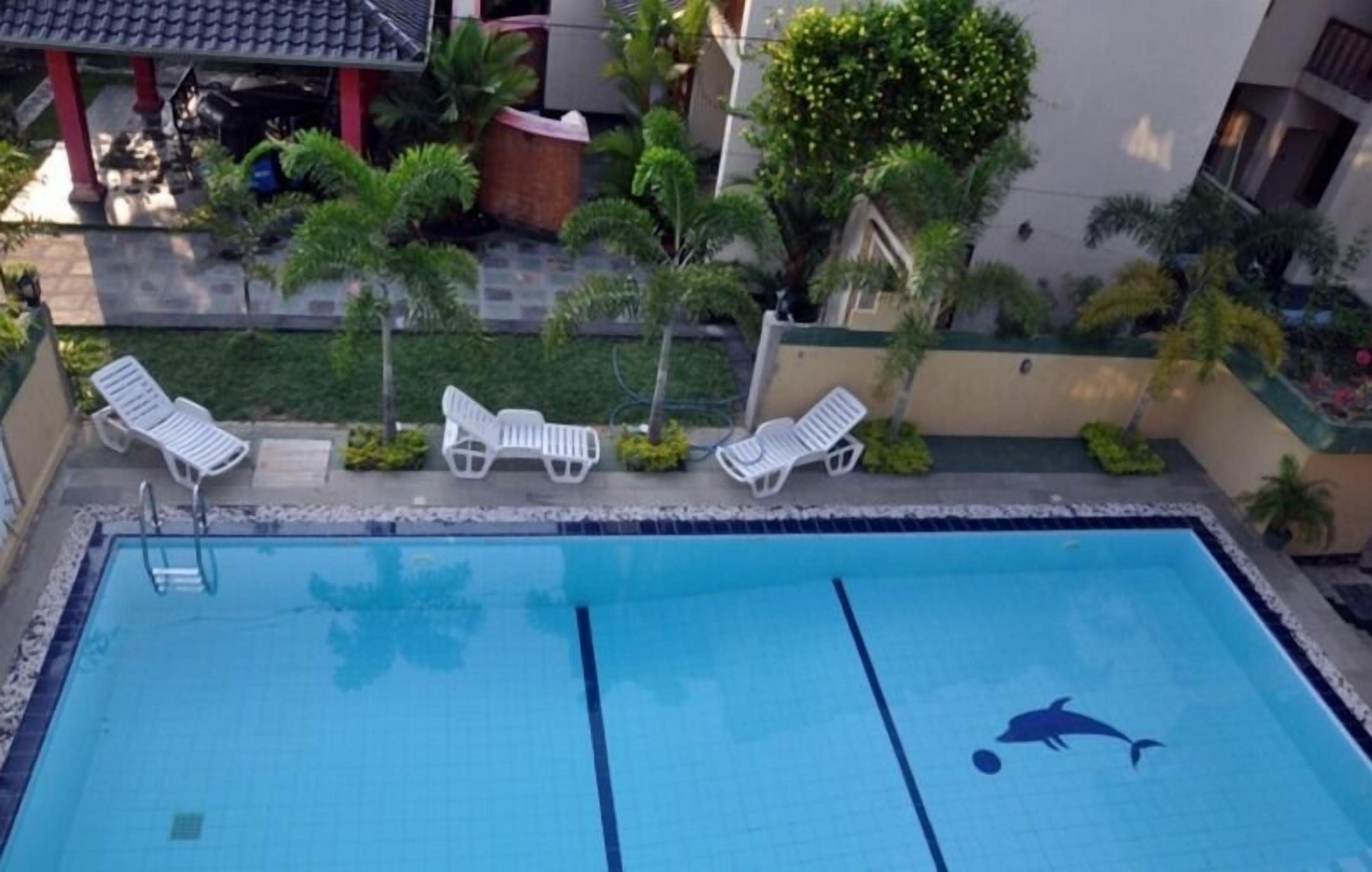 A swimming pool with a dolphin design, surrounded by white lounge chairs and palm trees.