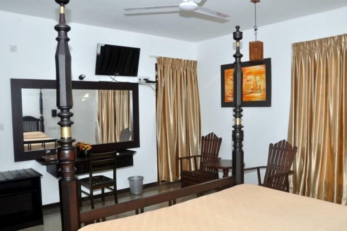 A bedroom with a four-poster bed, a ceiling fan, a television, and a large mirror.