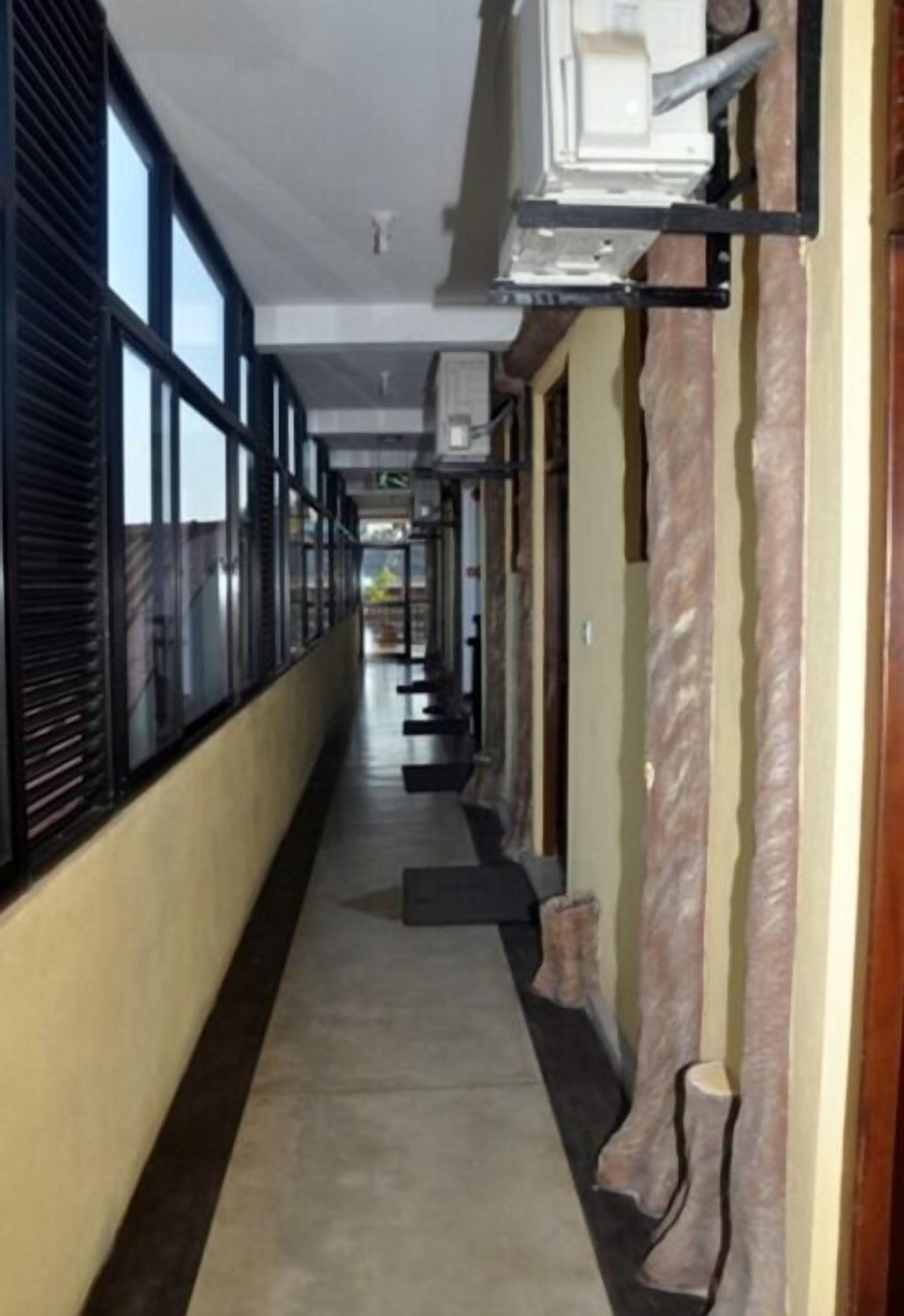 Un pasillo con ventanas amplias en un lateral, suelo de baldosas y una pared con textura similar al mármol en el otro lado.