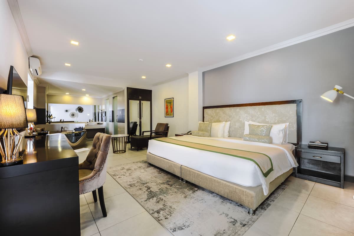 Ein Hotelzimmer mit Bett, Nachttischen, Schreibtisch, Stuhl und einem im Hintergrund sichtbaren Badezimmer.