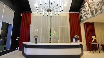 Un mostrador de recepción con una lámpara de araña moderna, cortinas rojas y un mural decorativo.