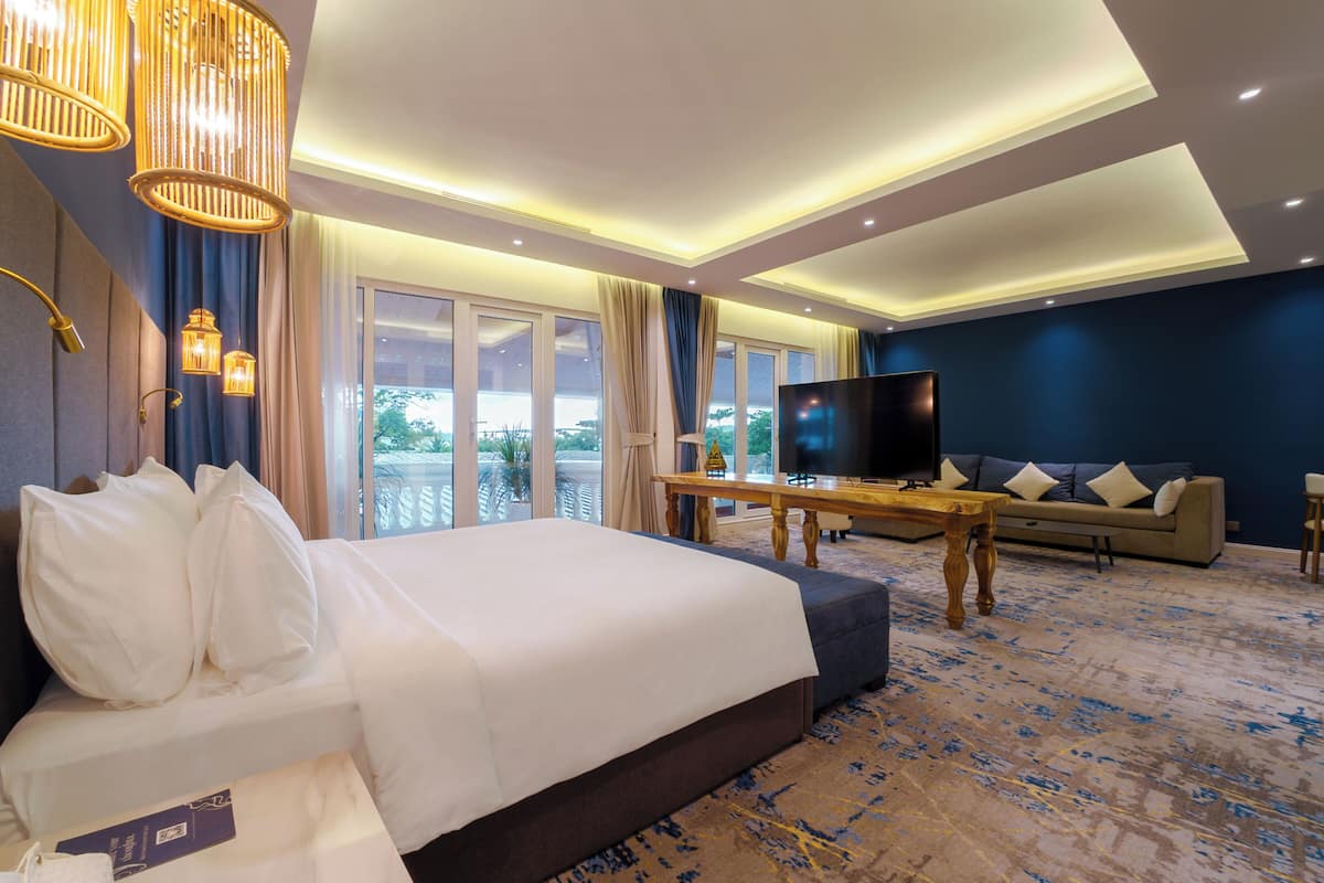 A hotel room with a large bed, a TV, a sofa, and a balcony with curtains.