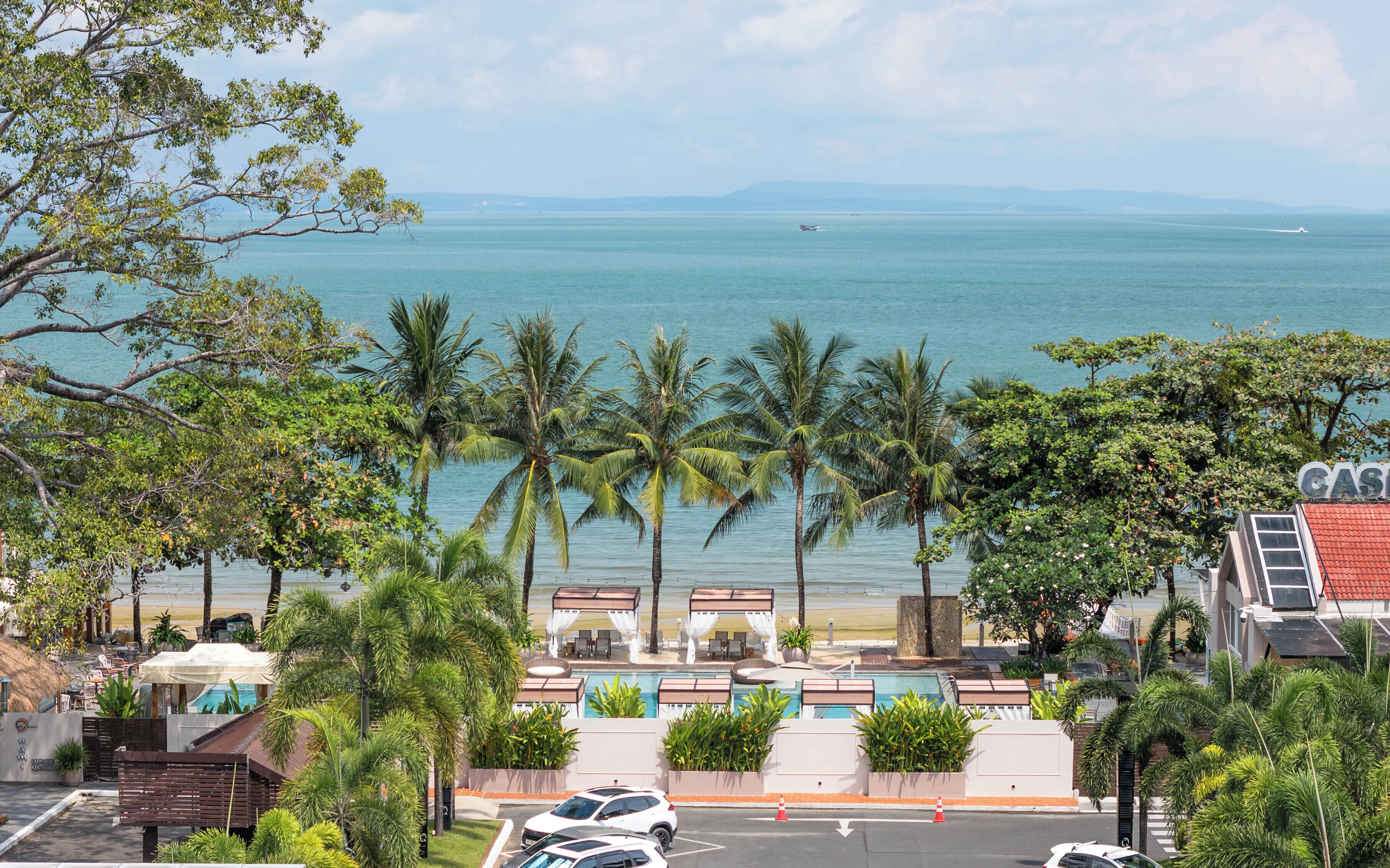 A hotel with a pool area, palm trees, and a view of the sea.