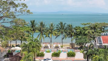 A hotel with a pool area, palm trees, and a view of the sea.