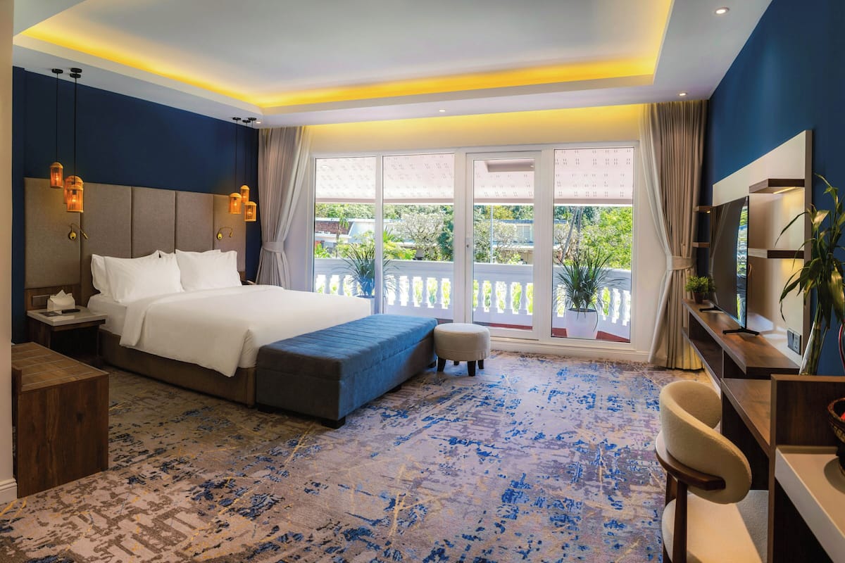 Ein Hotelzimmer mit einem großen Bett, einem Schreibtisch, einem Sessel, einem Fernseher und einem Balkon mit Blick.
