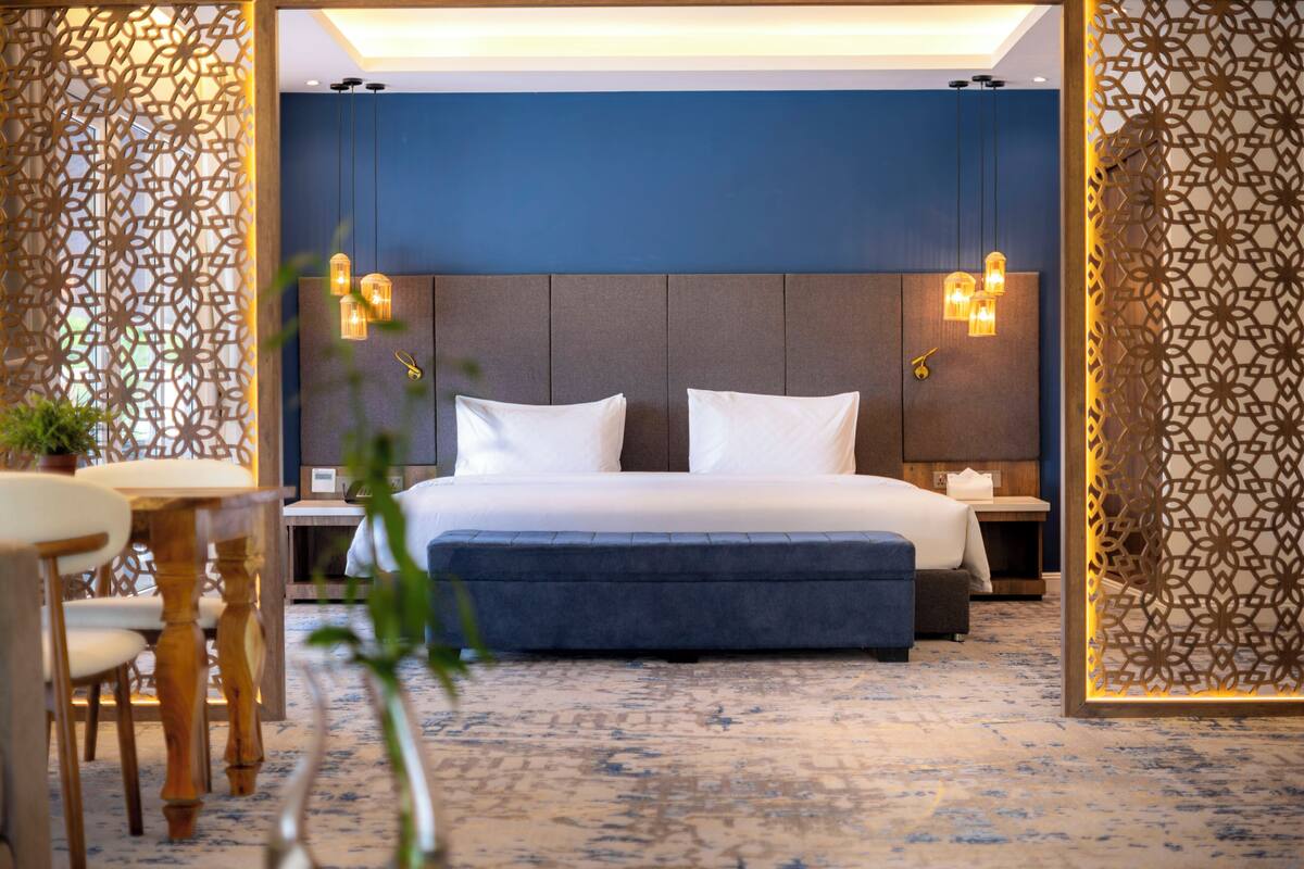 Ein Hotelzimmer mit einem großen Bett, Nachttischen, einem kleinen Tisch mit Stühlen und dekorativen Wandfeldern.