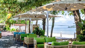 Buiten zitplaatsen met parasols, rieten meubels en uitzicht op het strand en water.