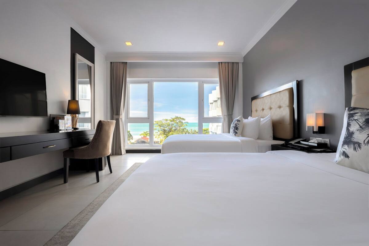 A hotel room with a large bed, a desk, a chair, a TV, and a view of the ocean.