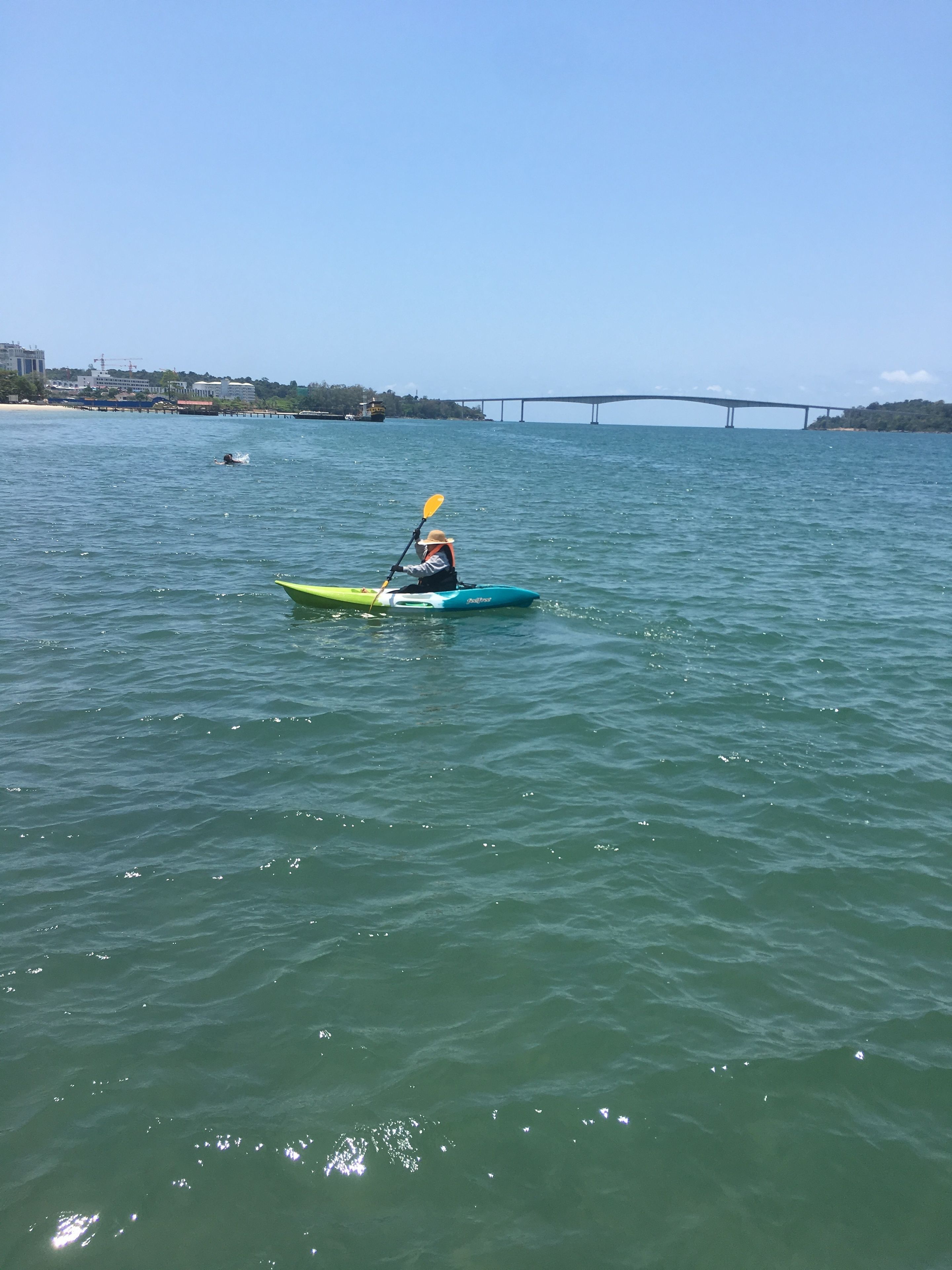 A kayaker on a calm body of water with a bridge and buildings in the background.