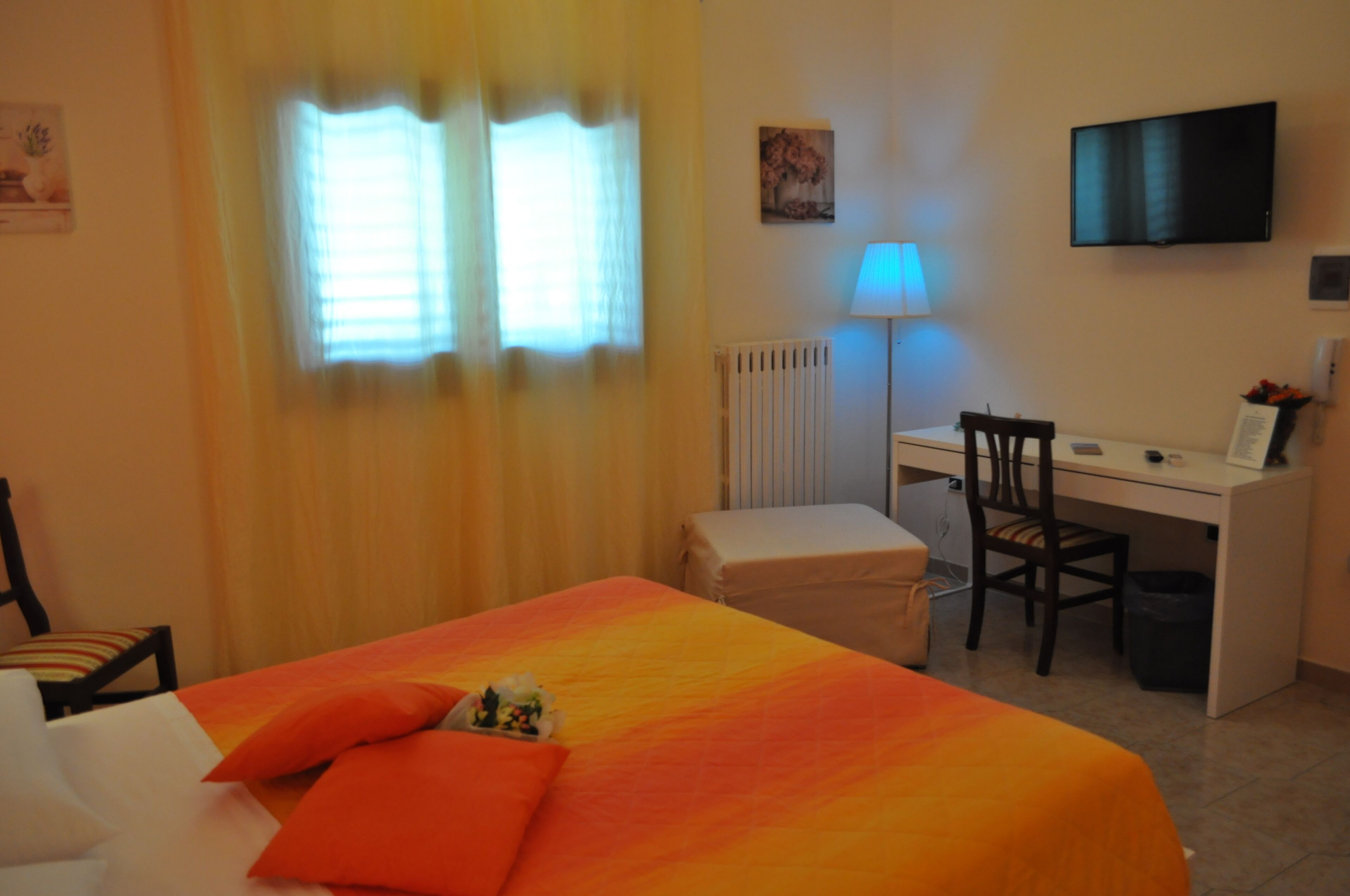 A hotel room with a bed, a desk, a chair, a TV, and a radiator.