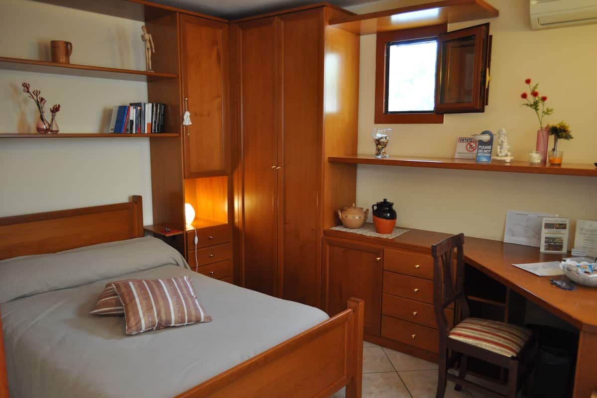 Ein Schlafzimmer mit einem Bett, einem Schreibtisch und einem Stuhl. Regale mit Büchern und Dekorationen.