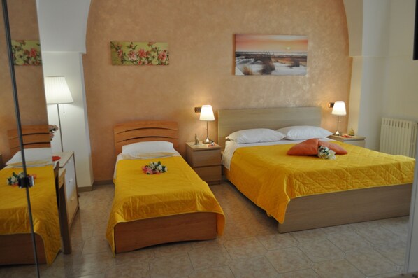 Habitación de hotel con dos camas individuales, cada una con cubrecama amarillo y almohadas blancas. Se observan mesitas de noche con lámparas, un cabecero de madera y un cuadro en la pared.