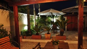 Un espace extérieur aménagé en terrasse, avec des bancs et des tables en bois, entouré de plantes en pot et de parasols.