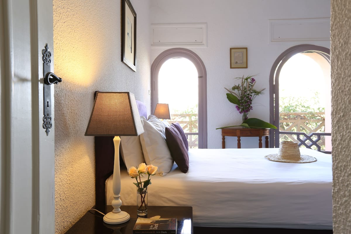 A bedroom with a bed, bedside table, lamp, and a vase with flowers.