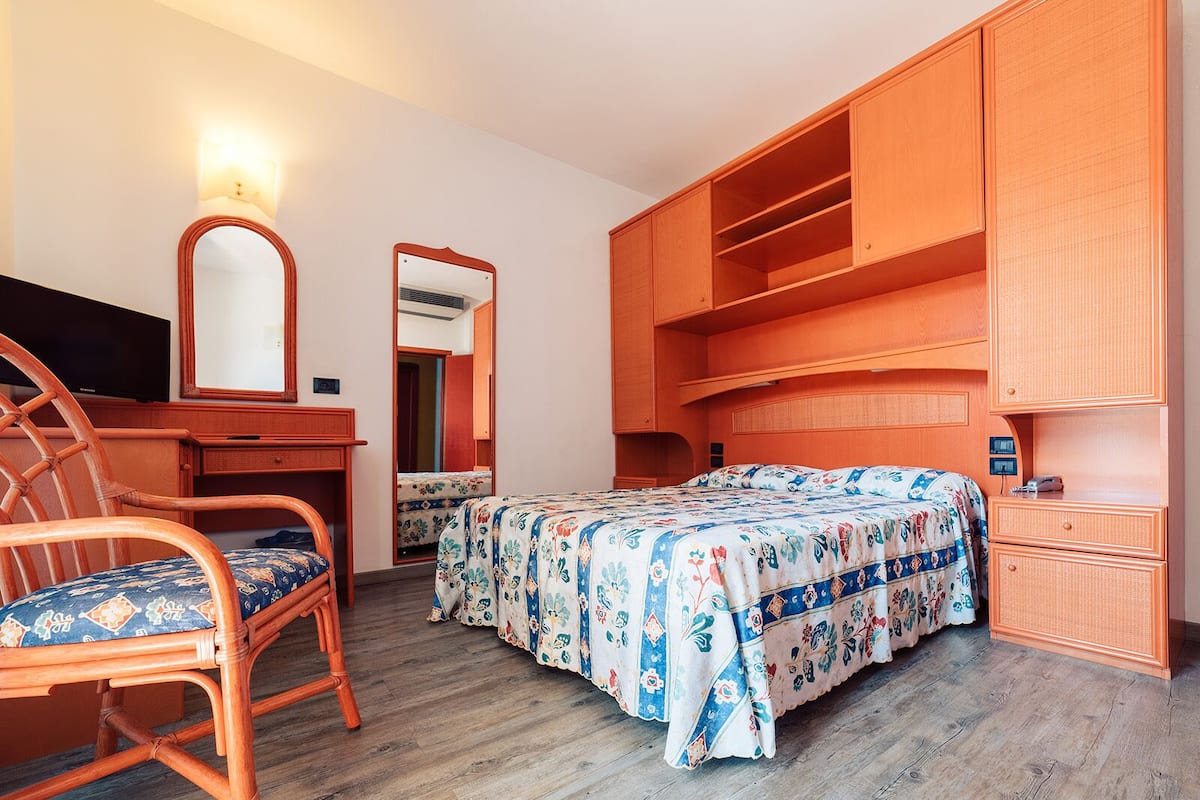 A bedroom with a bed, a desk, a chair, a wardrobe, and a mirror.