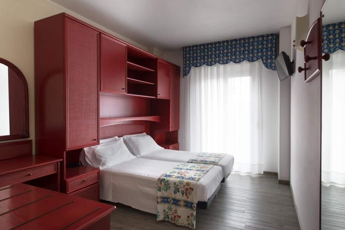 A room with two beds, a red wardrobe, a desk, and a mirror.