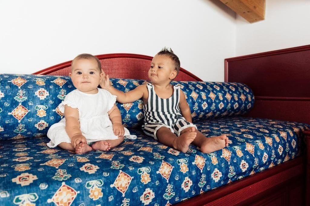 Dos niños sentados en un sofá estampado con un cabecero de madera.