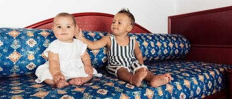Due bambini seduti su un divano a fantasia con una testiera in legno.