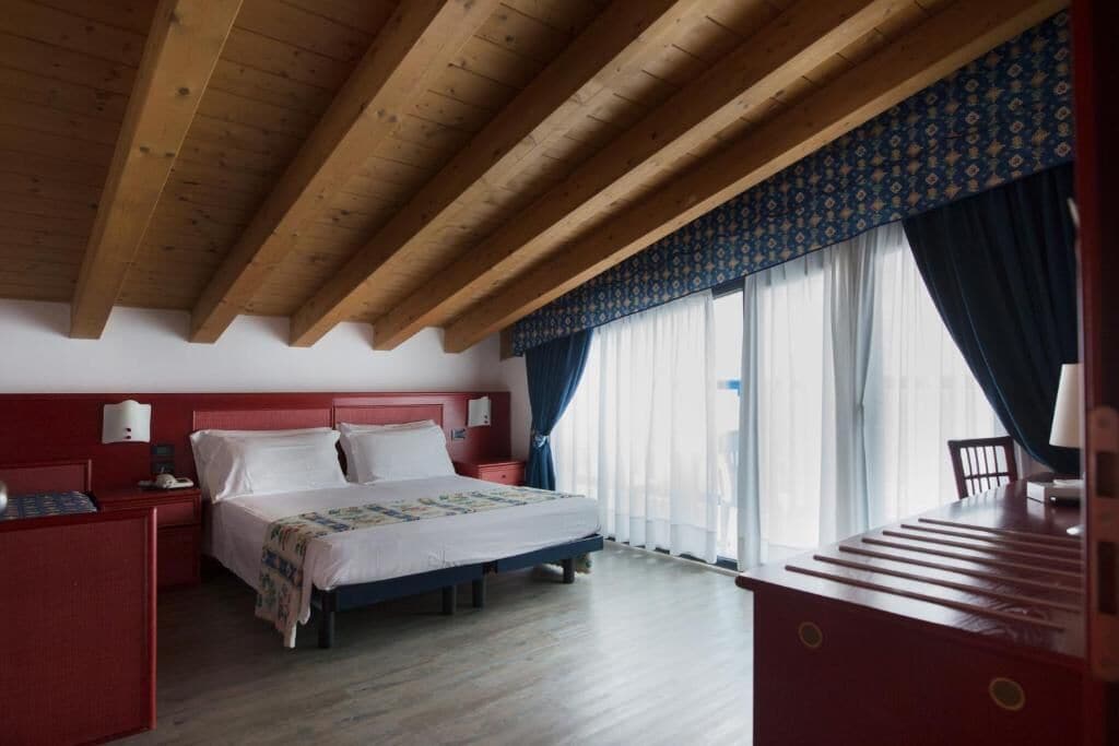 Een slaapkamer met een houten plafond, een bed met witte beddengoed, een rode nachtkastje en een bureau met een stoel.