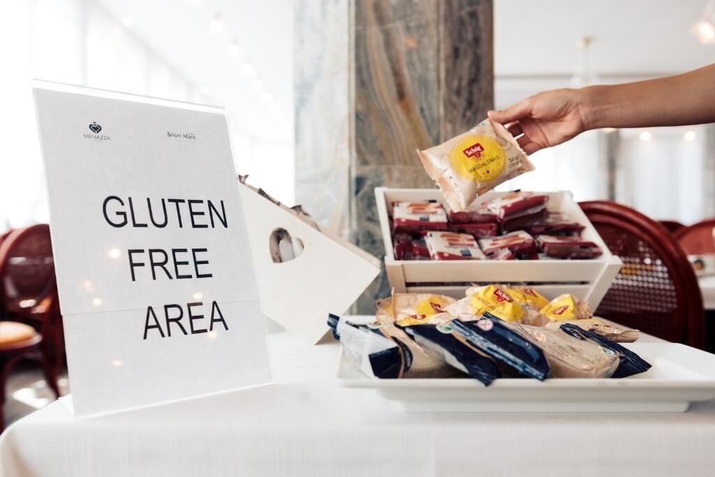 A sign indicating a gluten-free area, with a hand placing a gluten-free snack into a tray.