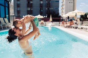 Une piscine avec des personnes, des chaises longues et des parasols.