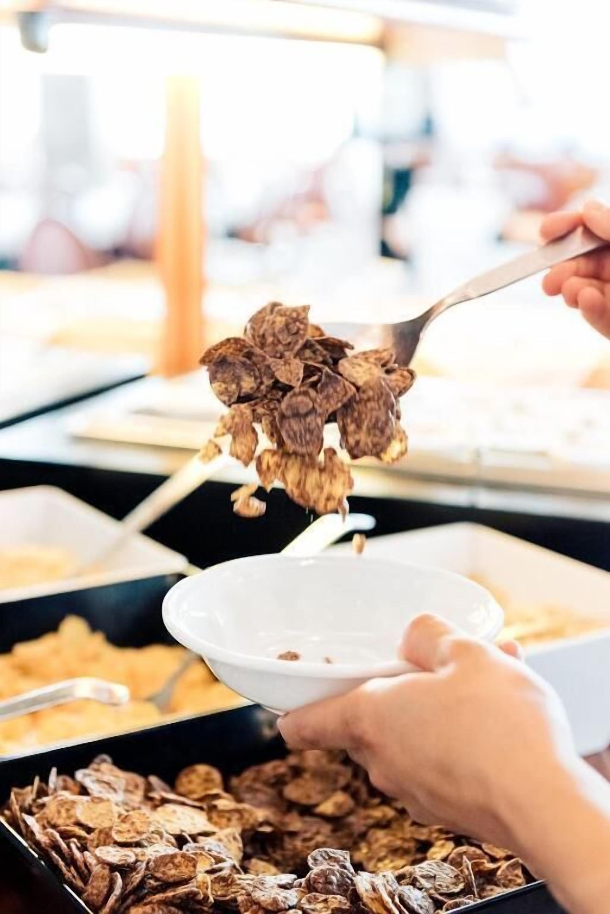 A person serving cereal from a bowl into a larger bowl.
