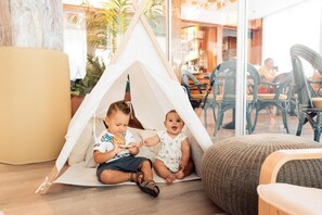 Two children playing inside a tent in a room with chairs and a table. - Hotel Brioni Mare (Jesolo)