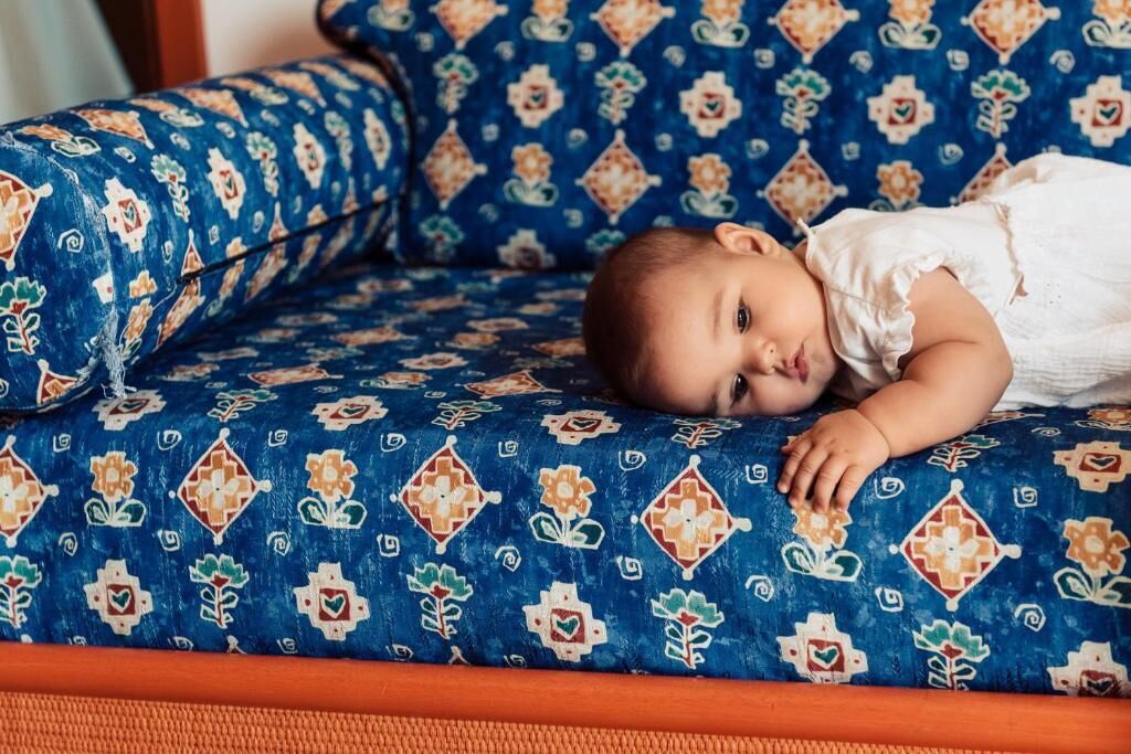 A child lying on a patterned sofa with a cushion.