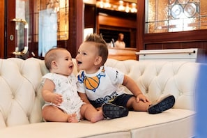 Two children sitting on a white tufted sofa in a room with wooden paneling and a large window with decorative glass. - Hotel Brioni Mare (Jesolo)