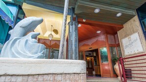 Entrada de un hotel con una gran escultura de piedra, una barandilla roja y un cartel que dice 'Hotel Brioni'.