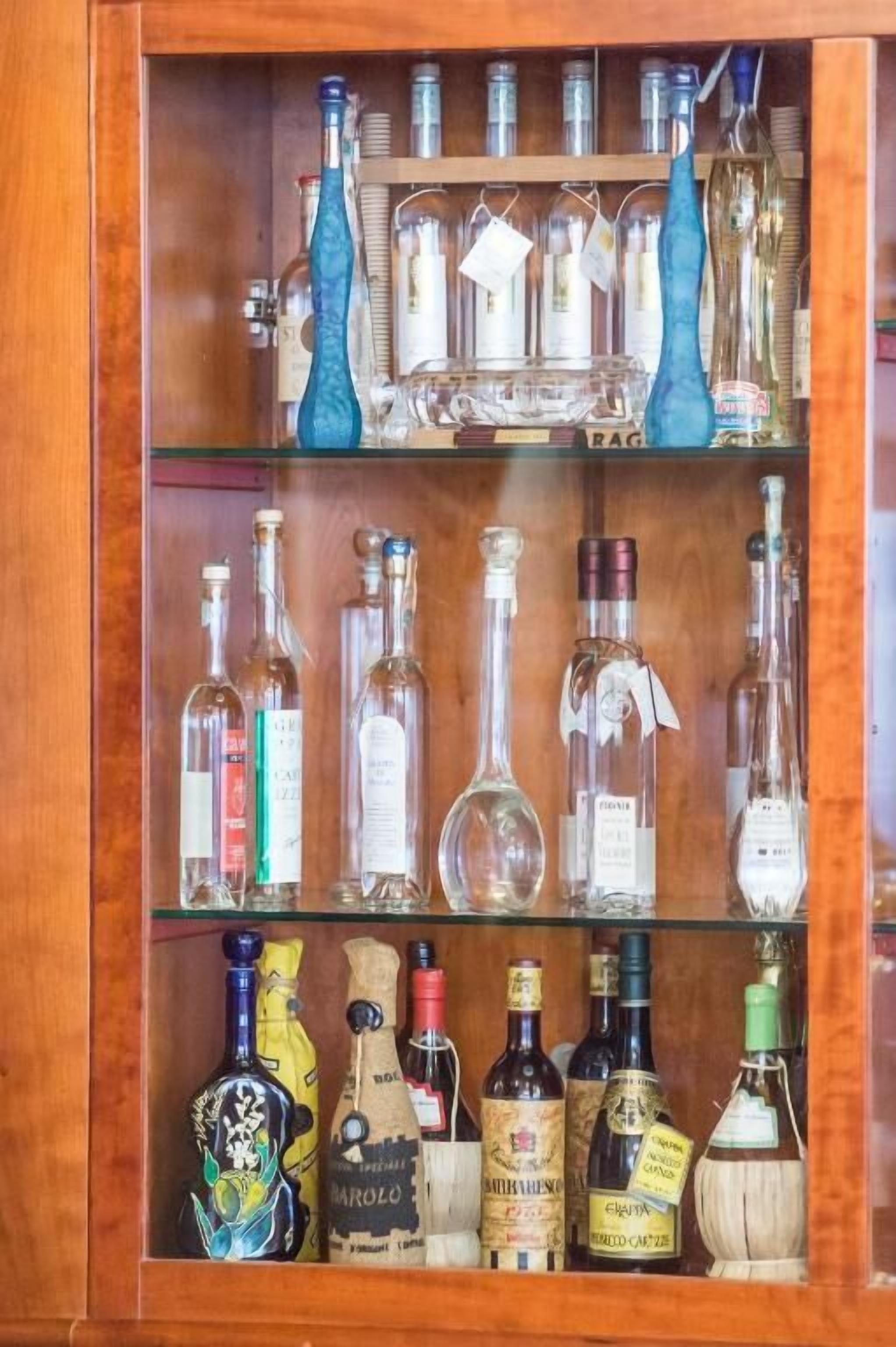 A wooden cabinet with three shelves containing various bottles of liquor.