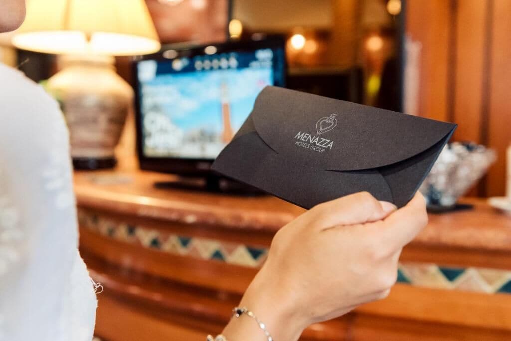A person holding a black envelope with the Menazza Hotels Group logo.