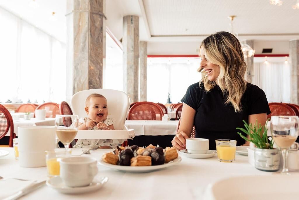 A dining area with a table set for two, including a high chair for a child, various dishes, and drinks.
