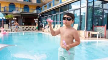 Una persona soplando burbujas junto a una piscina con un edificio al fondo.