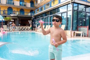 A person blowing bubbles by a swimming pool with a building in the background. - Hotel Brioni Mare (Jesolo)