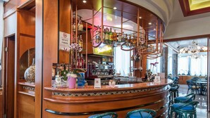 Zona de bar con un mostrador curvo de madera, taburetes acolchados azules y una variedad de botellas y vasos en estanterías.