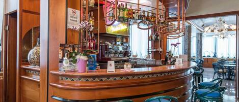 A bar area with a curved wooden counter, blue cushioned stools, and a variety of bottles and glasses on shelves.
