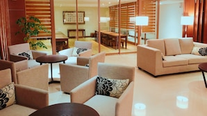 A modern hotel room with a seating area featuring sofas and armchairs, a dining table, and a large sliding glass door leading to a dining area. - WeMeet Hotel (Pingtung)