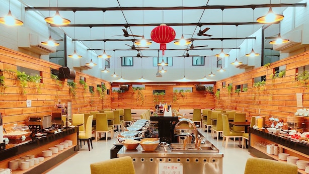 A restaurant with a long communal dining table, multiple chairs, and a buffet area with food and dishes. - WeMeet Hotel (Pingtung)