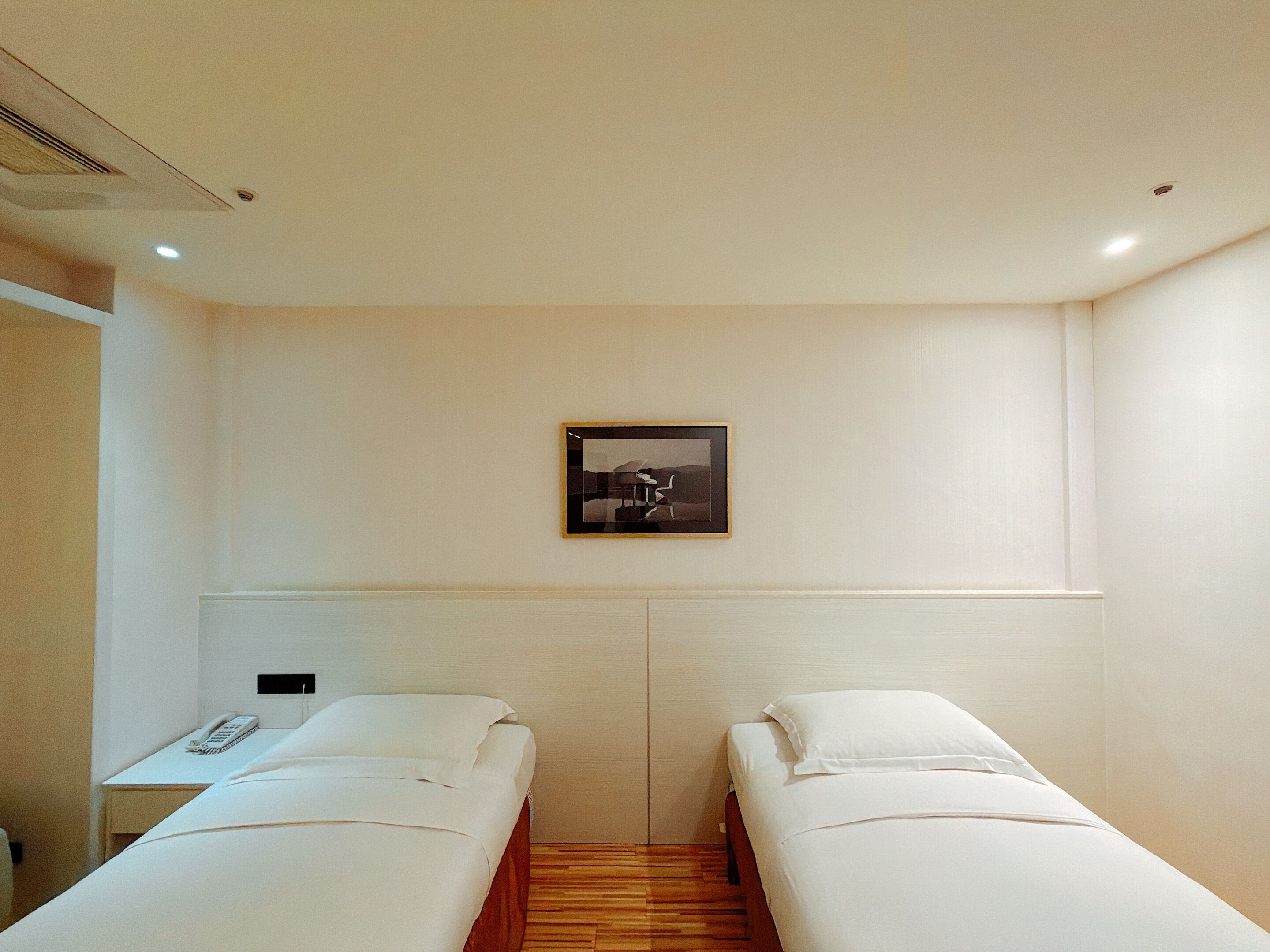A hotel room with two single beds, a small desk with a telephone, and a framed picture on the wall.